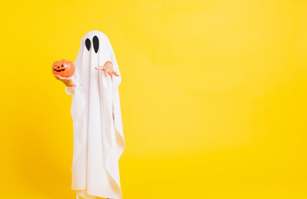 Foto niño con traje vestido de blanco fantasma de halloween tenebroso fantasma de calabaza naranja en la mano
