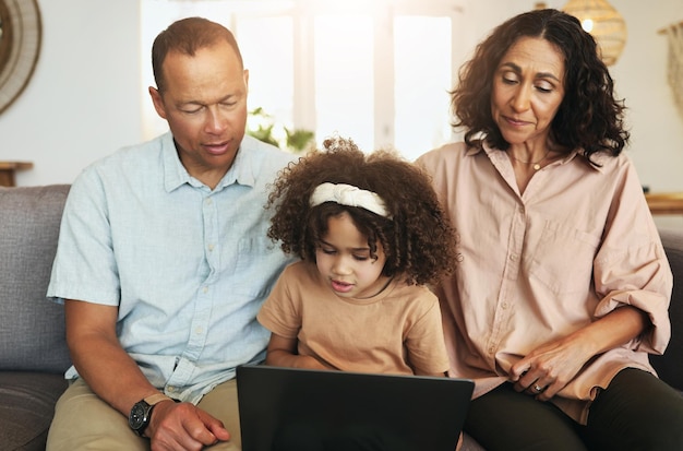 Niño transmitiendo una película en una computadora portátil con sus abuelos mientras se relaja en el sofá de la sala de estar Descanso tecnológico y niña viendo videos o películas con el abuelo y la abuela para entretenerse