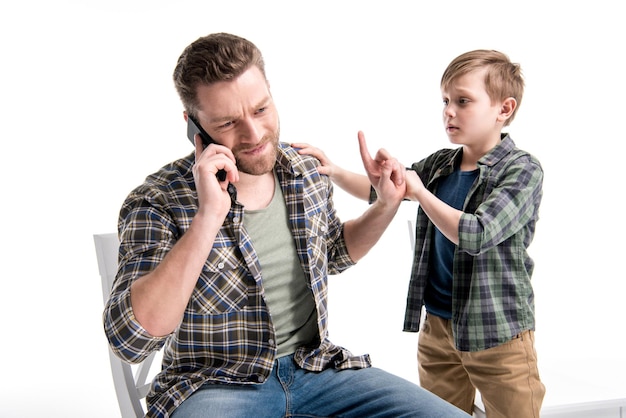 Niño tratando de hablar con el padre hablando por teléfono inteligente y gesticulando el concepto de problemas familiares