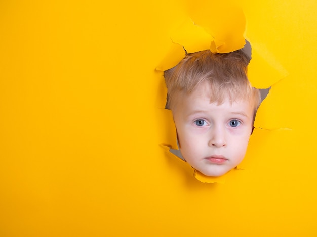 Niño a través de un agujero de papel amarillo pensando