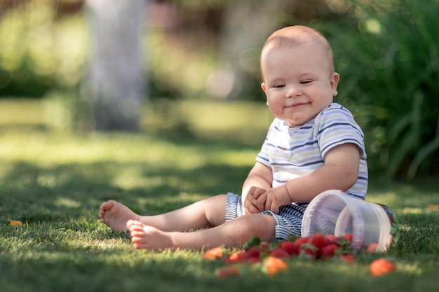 Niño travieso esparció fresas en la hierba y sonríe