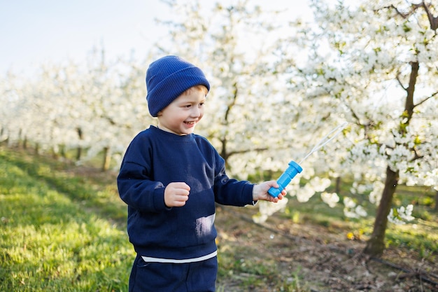 Un niño de tres años corre a través de un jardín floreciente con pompas de jabón. Un niño alegre y emotivo camina por el parque. Barras de jabón para niños.