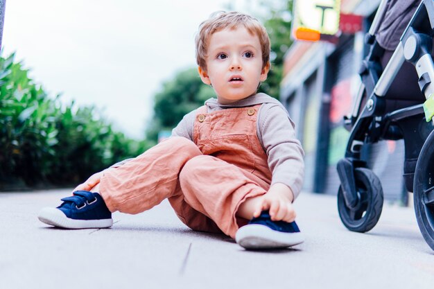 Niño de tres años con gesto de sorpresa sentado en la calle en un día fresco