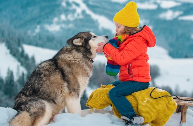 Niño en trineo disfrutando de un paseo en trineo niño sentado en el trineo con perro husky siberiano los niños juegan