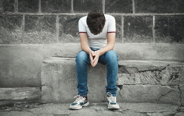 Niño triste caucásico sentado en la calle.