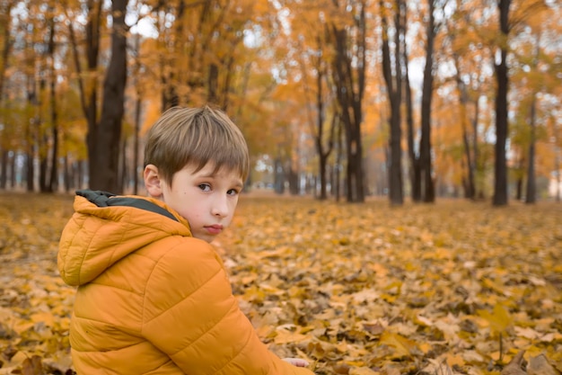 Un niño triste en el parque de otoño Un niño paseando en un día nublado y lluvioso