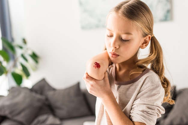 Niño triste que sopla en la herida en casa