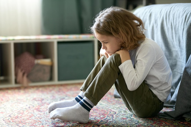 Un niño triste sentado en el suelo de su dormitorio y sintiéndose solo