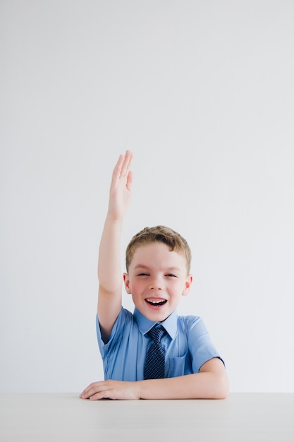 Niño en uniforme escolar levanta la mano en el escritorio