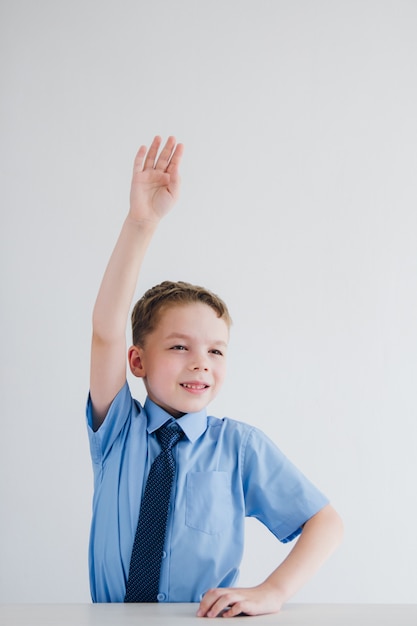 Niño en uniforme escolar levanta la mano en el escritorio