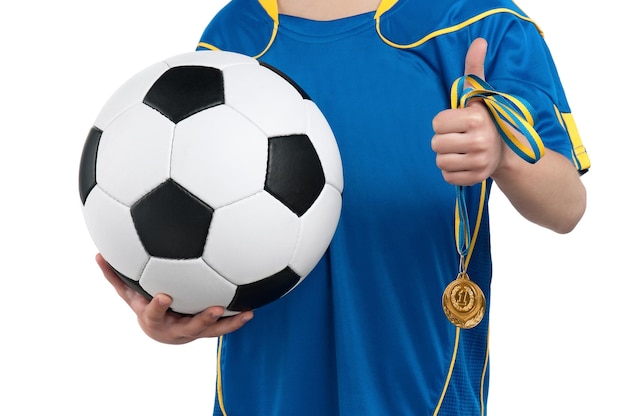 Niño en uniforme de fútbol nacional ucraniano con una pelota de fútbol clásica y una medalla en un fondo blanco aislado