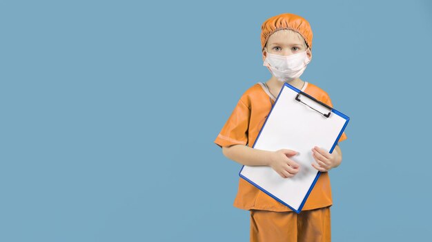 Un niño con uniforme de médico con máscara en una carpeta en sus manos