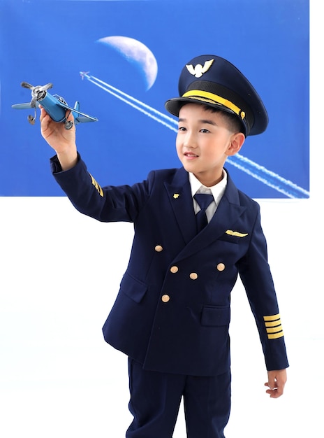 Un niño con uniforme de piloto sostiene un avión de juguete frente a una imagen de una luna.