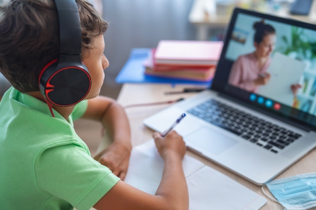 Foto niño usa laptop para hacer videollamadas con su maestra