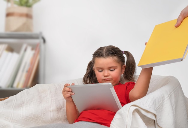 Un niño usa una tableta y rechaza un libro que le dio un adulto