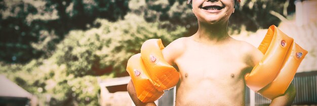 Niño usando brazaletes de pie junto a la piscina