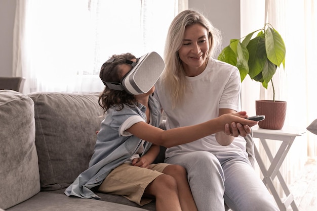 Niño usando casco de realidad virtual con su madre gafas vr en la sala de estar en casa divirtiéndose