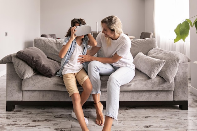 Niño usando casco de realidad virtual con su madre gafas vr en la sala de estar en casa divirtiéndose