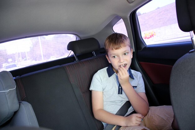 Foto el niño está usando un cinturón de seguridad sentado en el asiento trasero del coche come comida retrato en primer plano