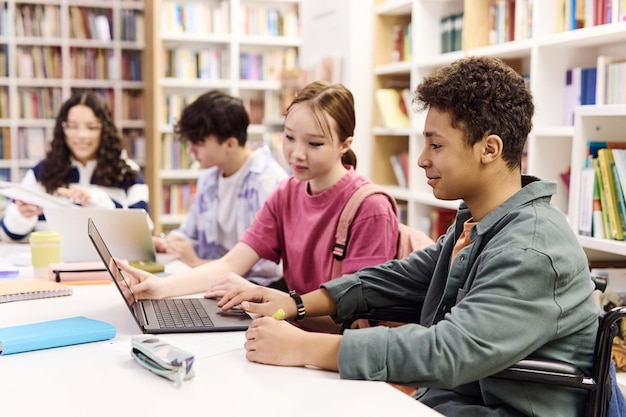 Niño usando la computadora en la biblioteca con un grupo diverso de estudiantes