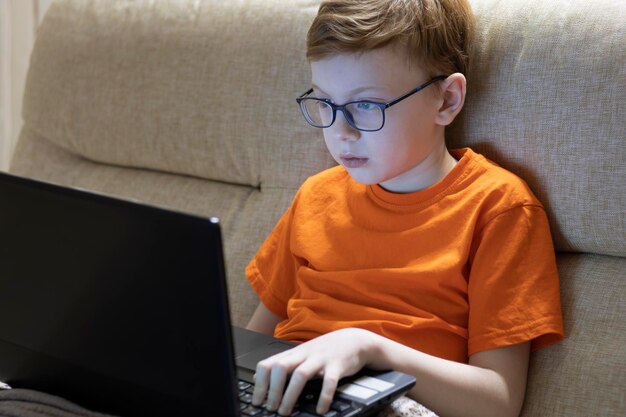 Niño usando una computadora portátil sentado en el sofá en casa