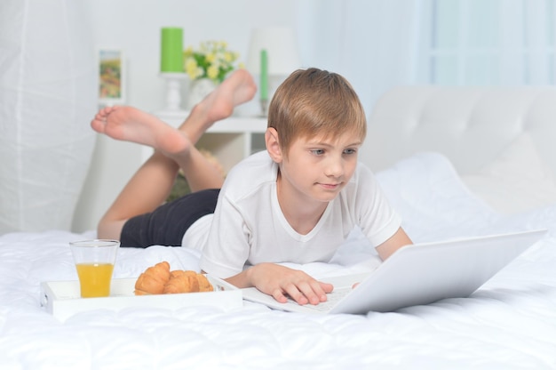 Niño usando una laptop en la cama mientras desayuna