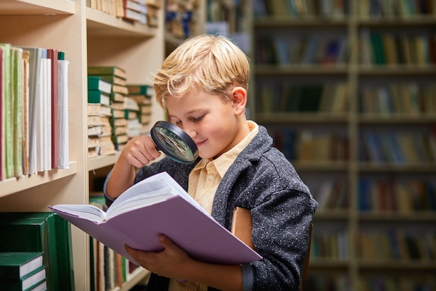 niño usando lupa para leer, obtener nueva información para el cerebro en la biblioteca