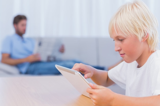 Niño usando la pc de la tableta mientras su padre está leyendo