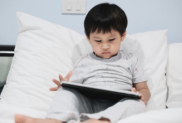 Un niño usando una tableta en casa en el dormitorio.