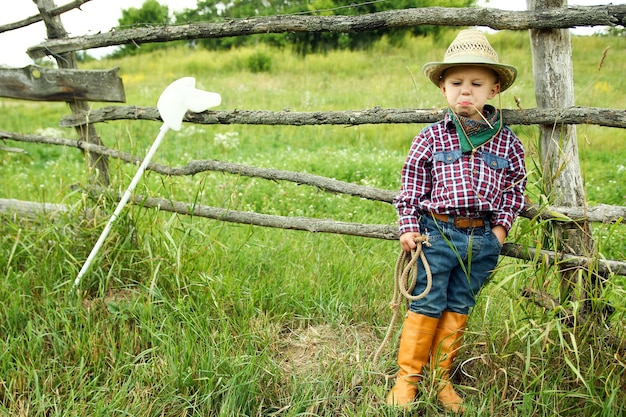 Un niño vaquero con sombrero con cuerda y caballo de juguete en la naturaleza