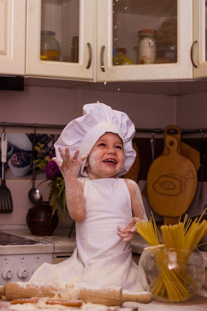 Foto niño vestido como un cocinero amasa la masa de harina
