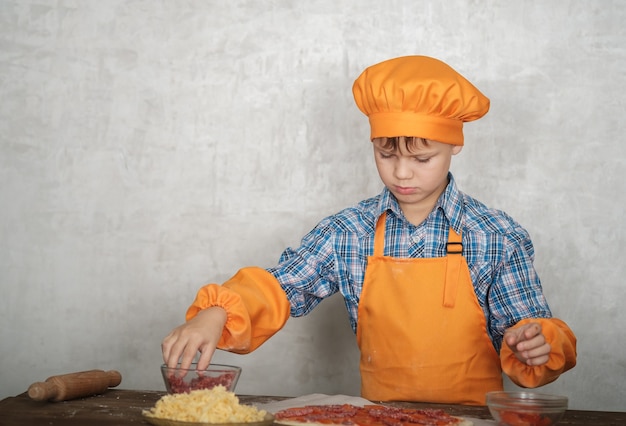 niño vestido como cocinero se dedica a cocinar pizza casera