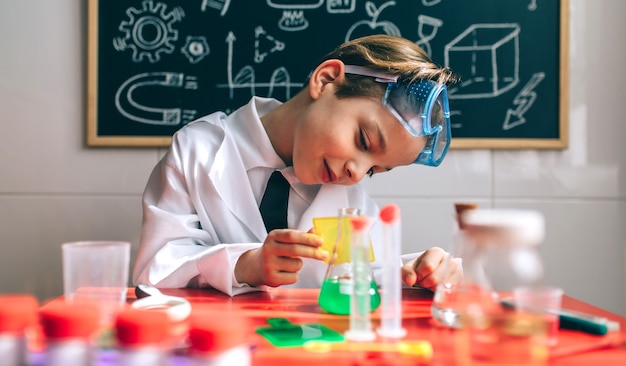 Niño vestido de químico jugando con juego de química frente a una pizarra con dibujos