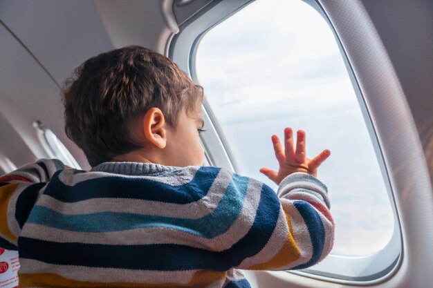 Niño viajando en avión de vacaciones mirando por la ventana viendo despegar