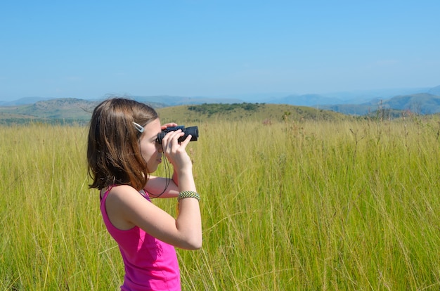 Niño en un viaje de safari en África, niña mirando a la sabana con binoculares