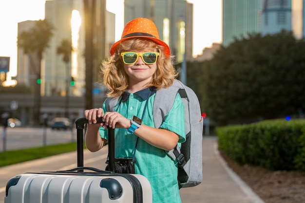 Niño viajero de pie y sosteniendo maleta al aire libre Niño turista que tiene un viaje de vacaciones alegre Viaje de niño con bolsa de viaje Niño con maleta sueña con viajar vacaciones de aventura