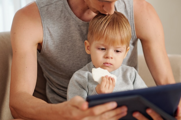 Niño viendo dibujos animados en tableta digital mientras está sentado junto con su padre