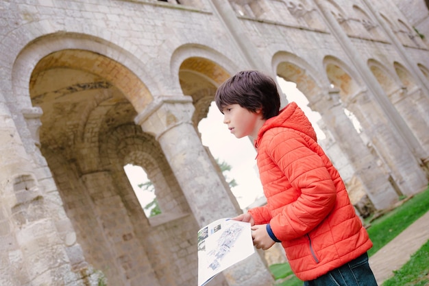 Niño visitando las ruinas del monasterio Abbaye de Jumieges en Normandía Francia Boy holding museo plan en sus manos