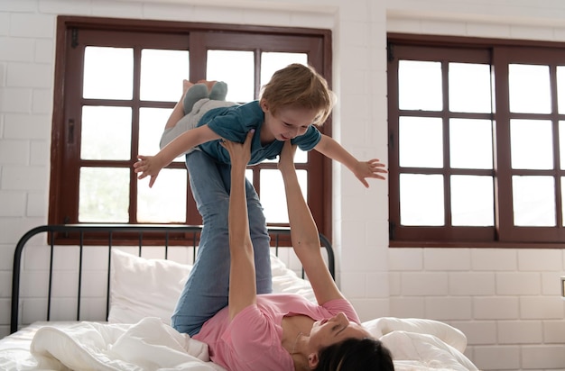 Niño volando con mamá usando sus piernas para ayudarlo a volar alto del suelo de su cama