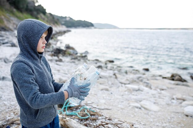 Foto niño voluntario limpia plástico y basura con bolsa de basura en el concepto de ecología de la costa