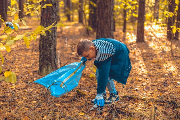 Un niño voluntario recoge residuos plásticos en una bolsa de basura Un niño activista ecológico salva el bosque de