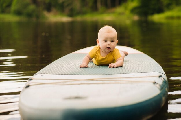 El niño yace flotando en el agua en una tabla sup grande Deportes acuáticos