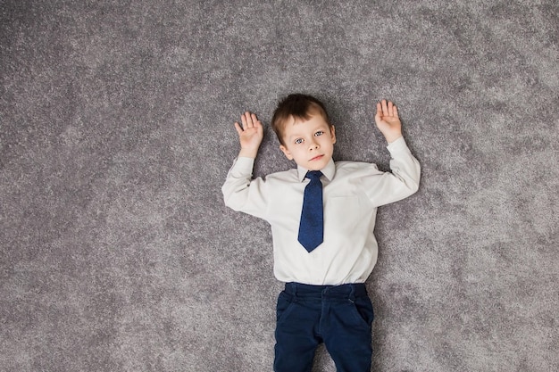 El niño yace en el suelo. Niño acostado en el piso de la alfombra en casa y sonriendo. Niño Acostado Sobre La Alfombra. Niño Sonriente Feliz, Niño De Cinco Años. Vista superior del niño pequeño mientras está acostado en el suelo.