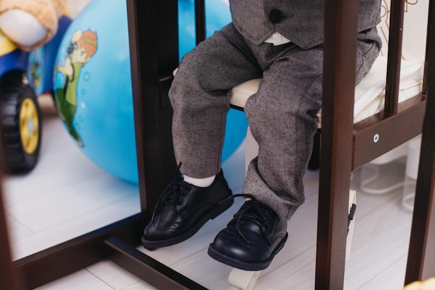 Un niño con zapatos negros se sienta en una silla con un globo terráqueo a un lado.