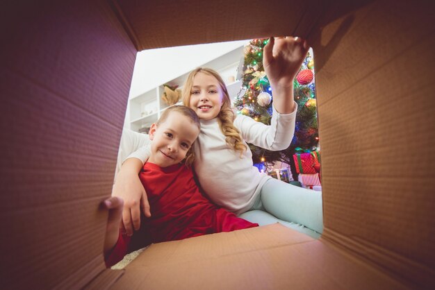 Los niños abren la caja cerca del árbol de navidad.