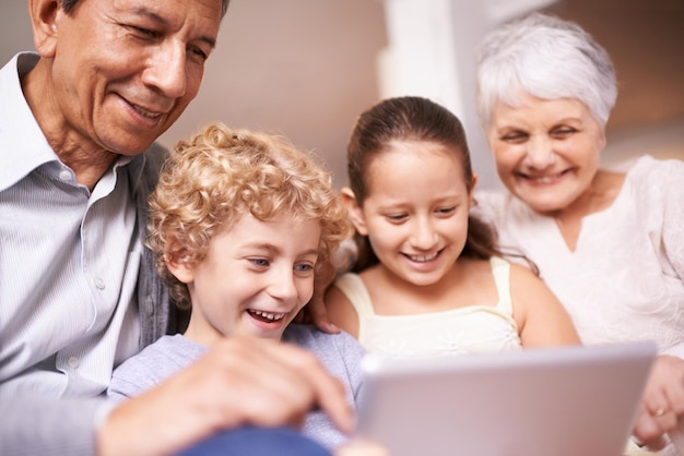 Niños con abuelos Una foto de dos niños y sus abuelos usando una tableta digital mientras están sentados en el sofá