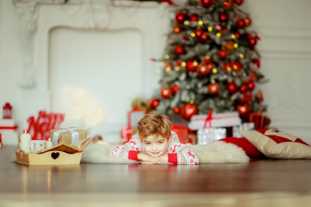 Niños acostados sobre una alfombra hecha de pieles naturales en pijama rojo debajo del árbol de Navidad