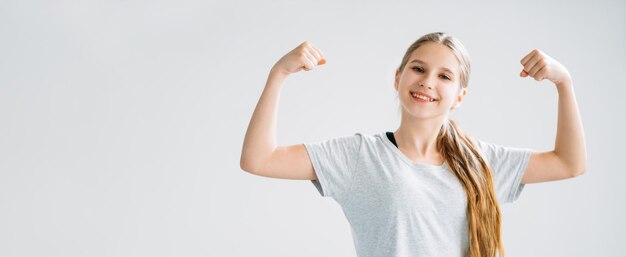 Niños activos Banner deportivo Entrenamiento físico Ejercicio matutino Feliz sonriente chica atlética fuerte en camiseta mostrando los músculos bíceps aislados en el fondo del espacio de copia ligera