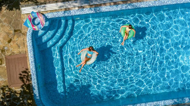 Niños activos en la piscina vista aérea desde arriba, niños felices nadan en rosquillas inflables y se divierten en el agua en vacaciones familiares en el resort