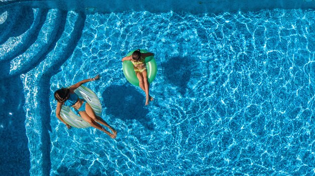 Niños activos en la piscina vista aérea desde arriba, niños felices nadan en rosquillas inflables y se divierten en el agua en vacaciones familiares en el resort